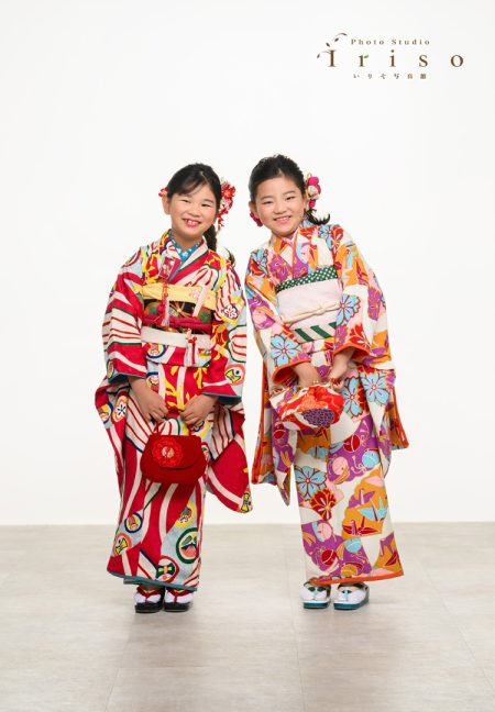 色鮮やかな和柄の着物を着た二人の女の子が笑顔で並んでいる姿。赤いバッグがアクセント。