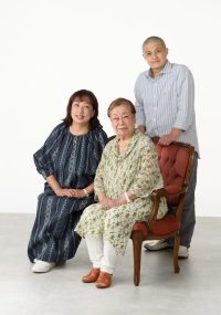家族写真で、全員が穏やかに笑顔を浮かべており、温かい家族の絆を感じさせるシーンとなっています。シンプルな背景が、家族の姿を引き立てています。