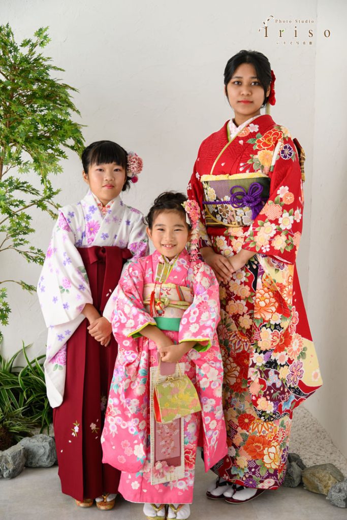 豪華な和装をまとった3人の女性が並び微笑む姿。姉妹が鮮やかな着物で記念撮影。