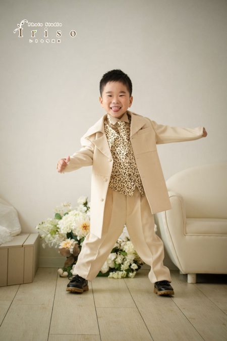 ベージュのスーツにレオパード柄のシャツを着た男の子が、元気いっぱいにポーズを取る姿。