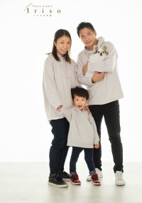 カジュアルな白いパーカーを着た家族が、小さな犬を抱えながらスタジオで笑顔を見せている写真。