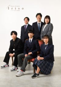 フォーマルなスーツと制服を着た家族6人が、椅子を中心に整列して撮影された記念写真。