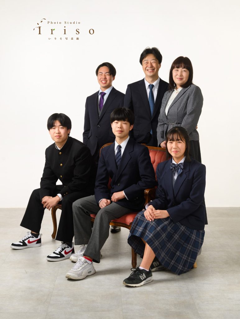 フォーマルなスーツと制服を着た家族6人が、椅子を中心に整列して撮影された記念写真。
