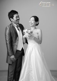 ウェディングドレスとタキシードを着た新郎新婦が、楽しそうに笑いながら寄り添うモノクロ写真。