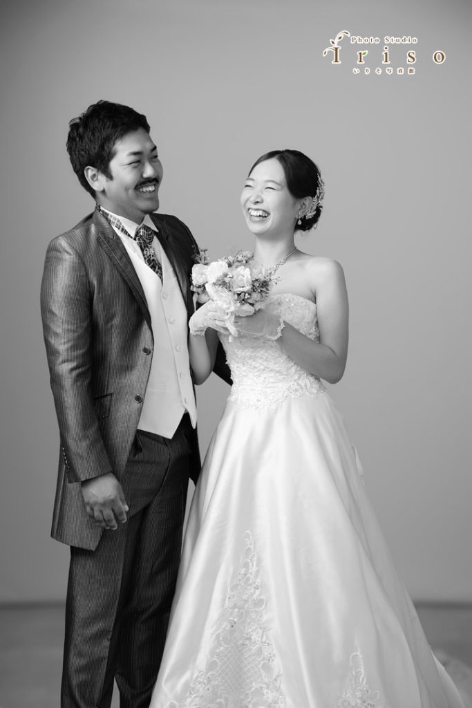 ウェディングドレスとタキシードを着た新郎新婦が、楽しそうに笑いながら寄り添うモノクロ写真。