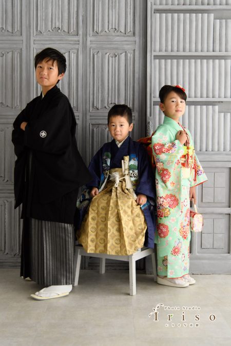 黒、金、ミントグリーンの和装を着た3人の子どもたちが、シックな背景の前で凛とした姿勢でポーズを取っています。