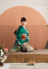 緑の花柄振袖を着た女性が、畳の上に正座して落ち着いた表情で撮影された写真。近くには草履とバッグが置かれています。