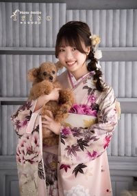 ピンクの華やかな振袖を着た女性が、小さなトイプードルを抱えながら笑顔を見せる写真。