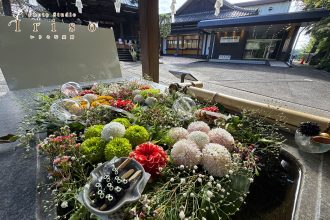 狭山の神社境内に美しく飾られた花々と、背景には伝統的な建物が広がる風景。おみくじや花装飾が和の趣を演出