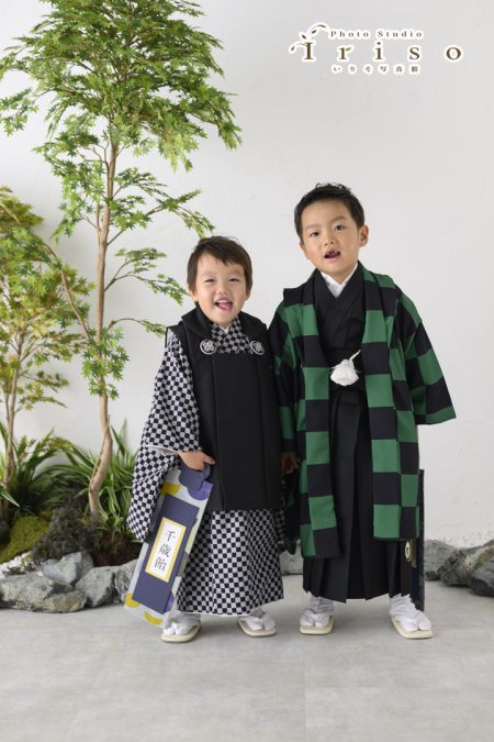 チェック柄の羽織袴を着た子どもと、緑と黒の市松模様の羽織を着た子どもが並んで笑顔で立っています。