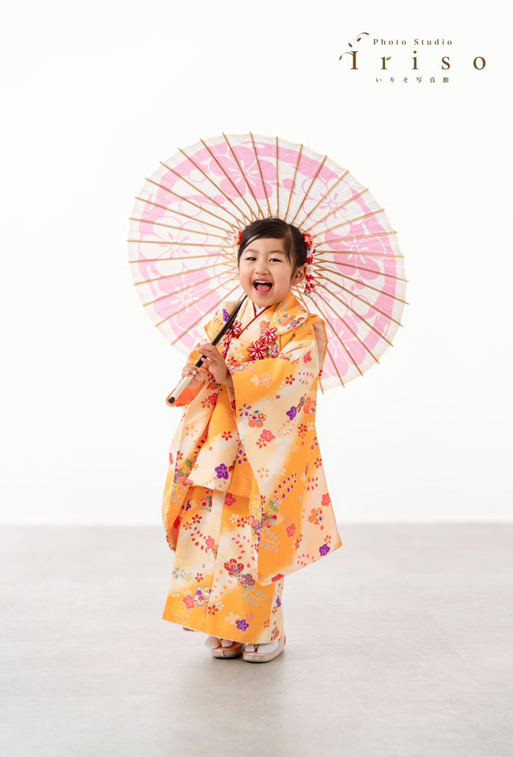 晴れ着姿でピンクの和傘を持つ女の子の写真。明るい黄色の着物がよくお似合いです！