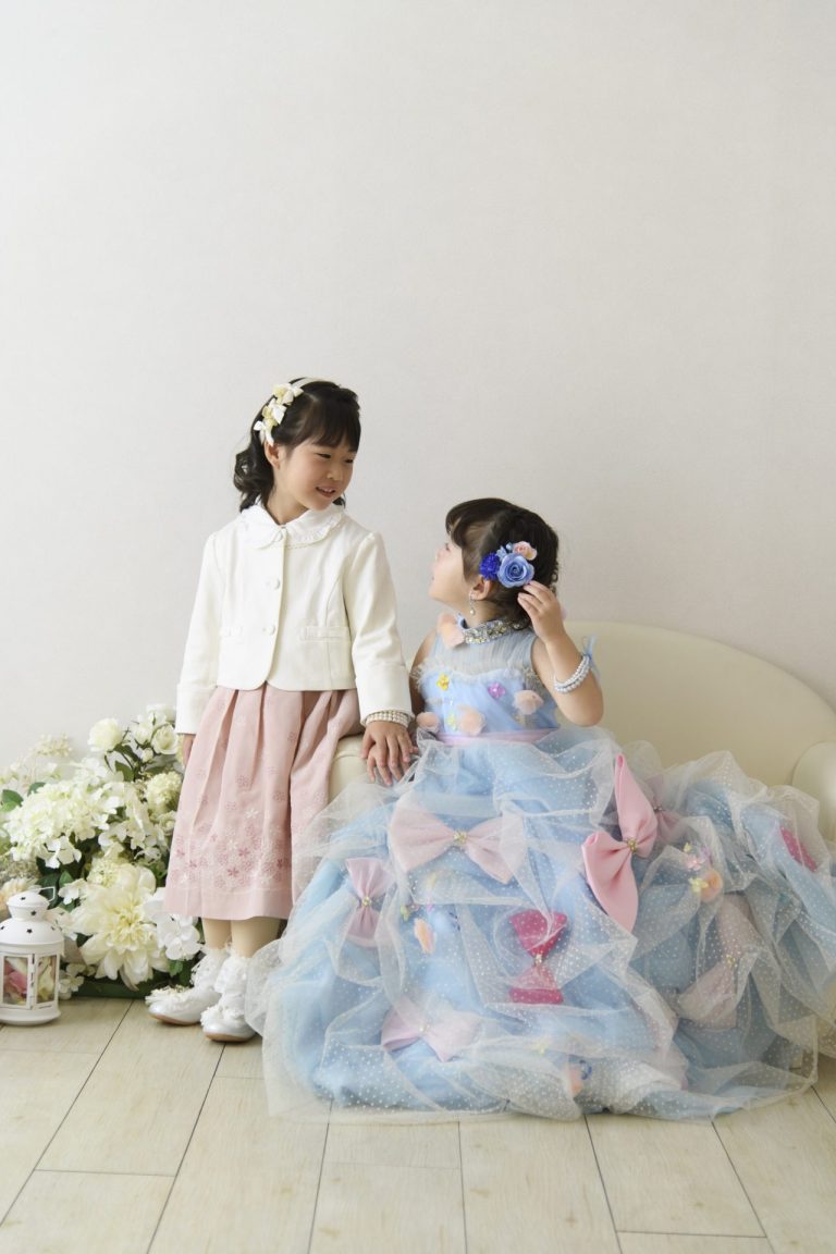 ピンクのドレスと水色のドレス、それぞれに合った衣装を身にまとった姉妹。お姉ちゃんは少しおすまし顔で、妹さんはお姉ちゃんのことが大好きな様子が伝わってくる笑顔。