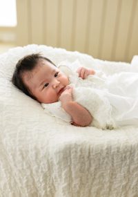 赤ちゃんが白いドレスを着て、白い布の上で寝ている写真。柔らかな白いドレスに包まれた赤ちゃん。まるで小さな天使が舞い降りてきたかのようです。スヤスヤと眠る姿は、見ているだけで心が温まります。