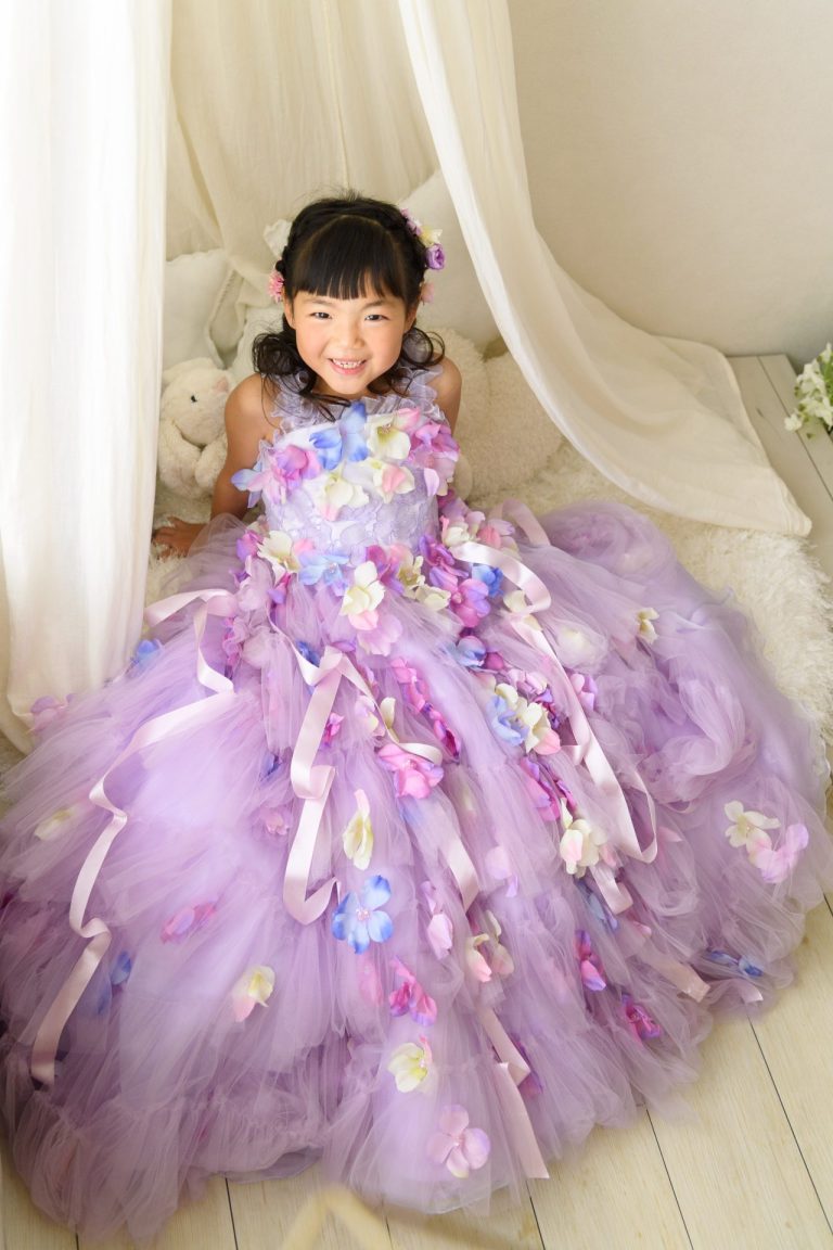 パステルパープルのドレスが、まるで満開のお花畑みたい！カラフルなお花とリボンが散りばめられたドレスは、女の子の可愛らしさをより一層引き立てています。ふんわりとしたチュールスカートも、夢のような雰囲気。