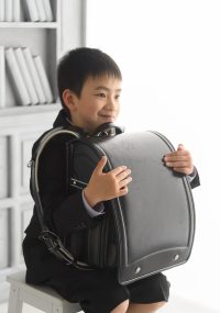ピカピカの大きなランドセルを両腕に抱えてほほ笑む男の子　ワクワクの表情をしています