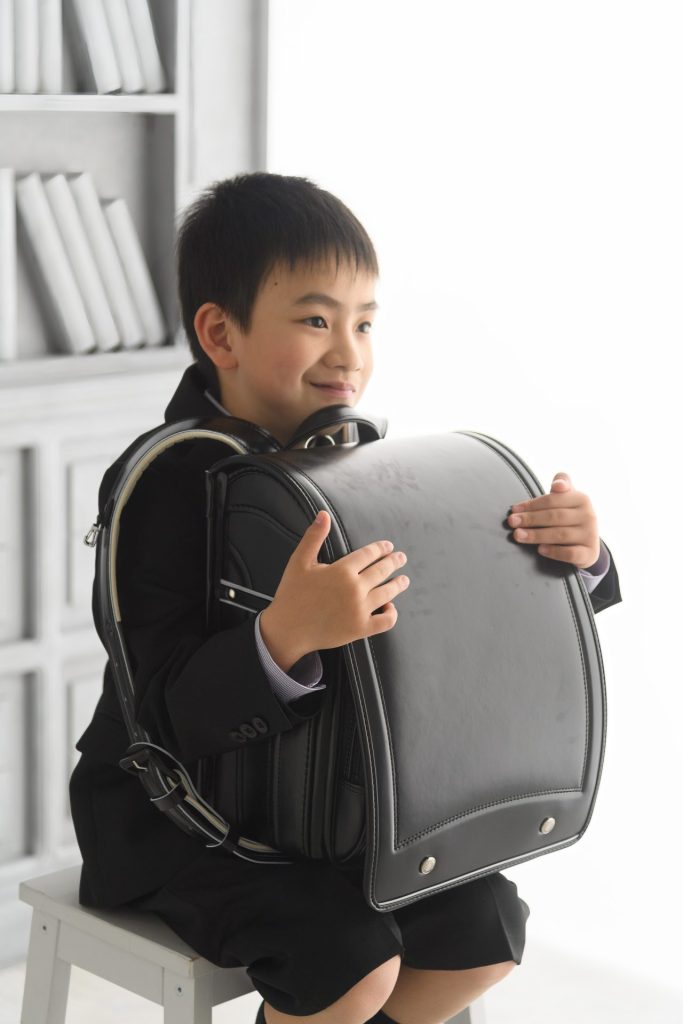 ピカピカの大きなランドセルを両腕に抱えてほほ笑む男の子　ワクワクの表情をしています