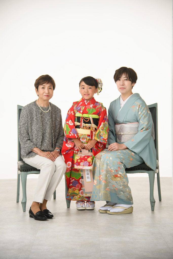 鮮やかな赤い着物に身を包んだ女の子と、優しい笑顔で見守るおばあちゃま、そして上品な着物姿のお母様。三世代揃っての記念写真は、この上なく華やかで、温かい雰囲気が溢れています。
