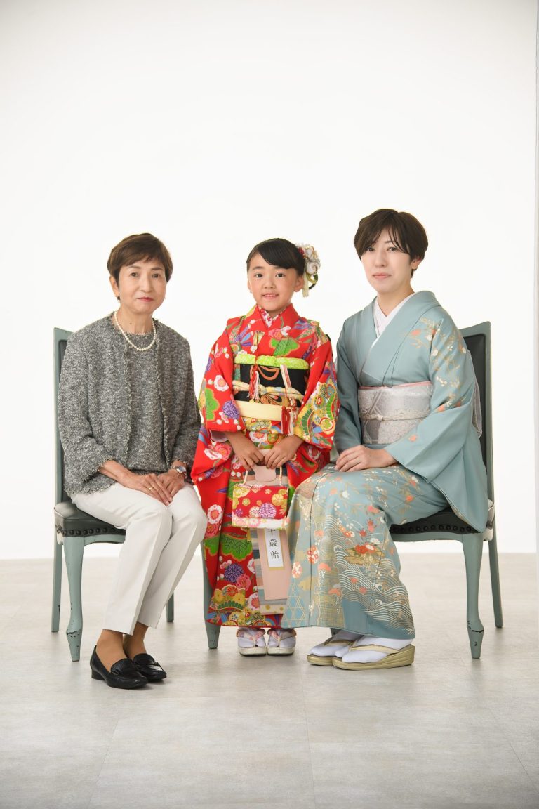 鮮やかな赤い着物に身を包んだ女の子と、優しい笑顔で見守るおばあちゃま、そして上品な着物姿のお母様。三世代揃っての記念写真は、この上なく華やかで、温かい雰囲気が溢れています。