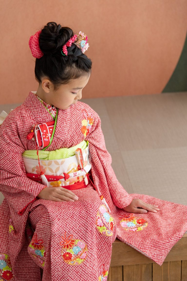 鮮やかな赤色の着物に身を包み、ちょっぴり緊張した面持ち。日本髪に飾られた髪飾りは、可愛らしさを一層引き立てています。