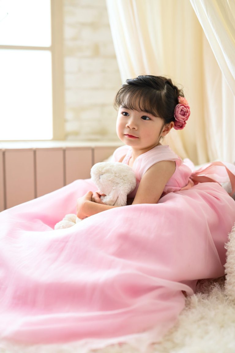 ピンクのドレスを着た女の子が白いぬいぐるみを抱えている写真。ふんわりとしたピンクのドレスが、彼女の可愛らしさを一層引き立てていますね。