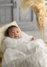 白いベビードレスの男の子が微笑んでいます