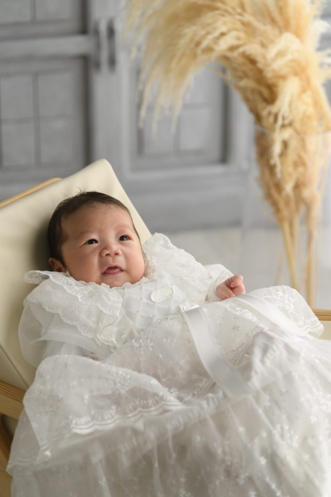 白いベビードレスの男の子が微笑んでいます
