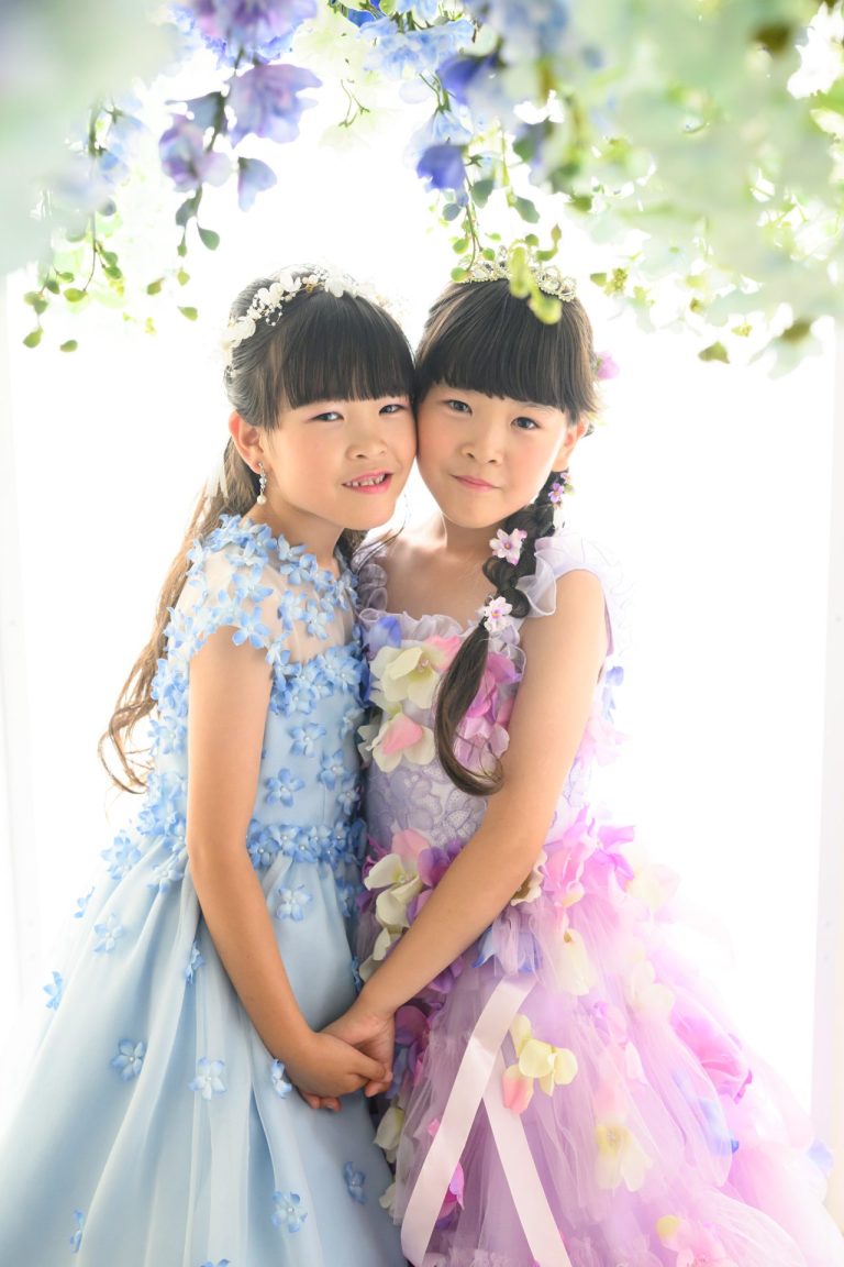 ドレスを着て花の下でほほを寄せ合う、仲の良い双子の女の子