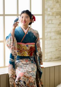 鮮やかな青い振袖をお召のお嬢様　お揃いの色の手乗りインコを見つめてほほ笑んでいます
