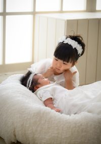 白いベビードレスの妹ちゃんを優しく見守るお姉ちゃん　お揃いのヘアーバンドが可愛い
