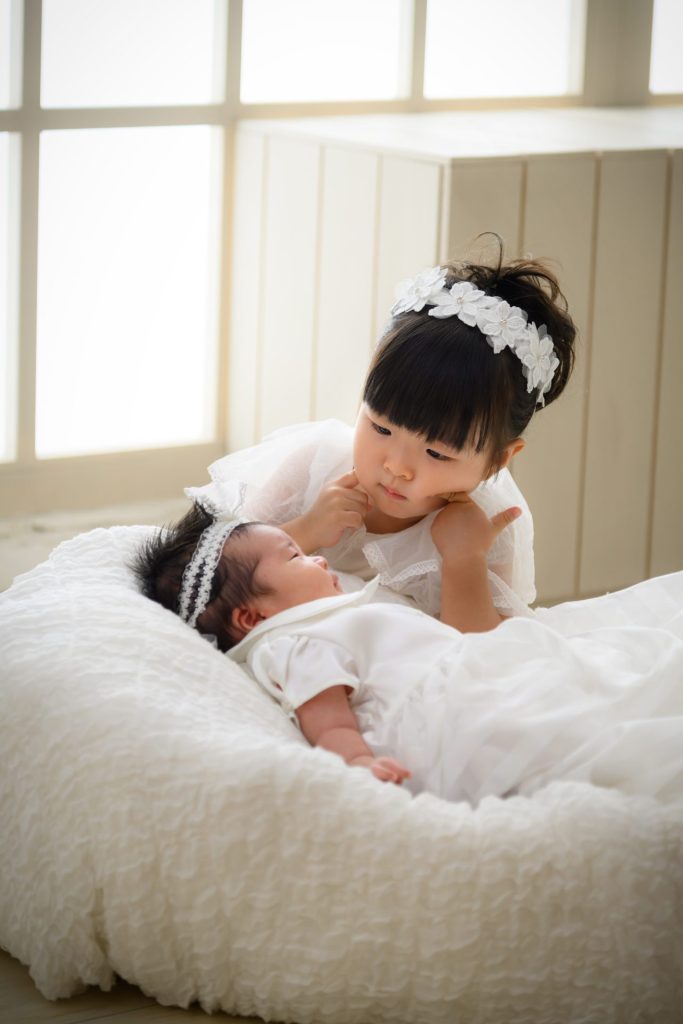 白いベビードレスの妹ちゃんを優しく見守るお姉ちゃん　お揃いのヘアーバンドが可愛い