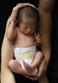 黒い背景に父と母の手に包まれた赤ちゃん
