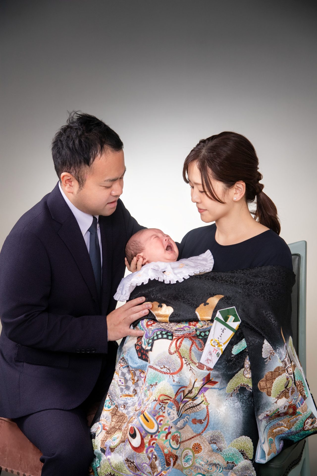 お祝い着を羽織った男の子を両親が見守っています
