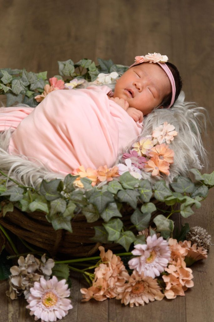 花に囲まれて、おくるみで眠る赤ちゃん