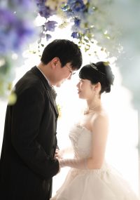 花のカーテンの下で見つめ合いほほ笑む新郎新婦様