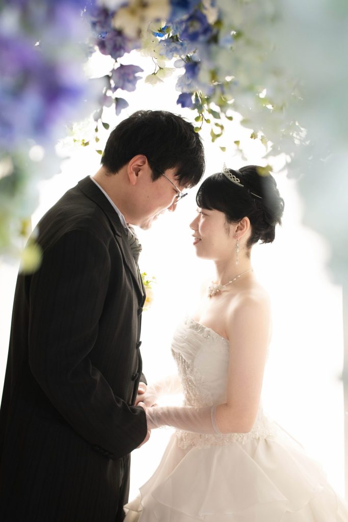 花のカーテンの下で見つめ合いほほ笑む新郎新婦様