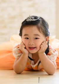 オレンジのドレスを着て頬杖でほほ笑む女の子
