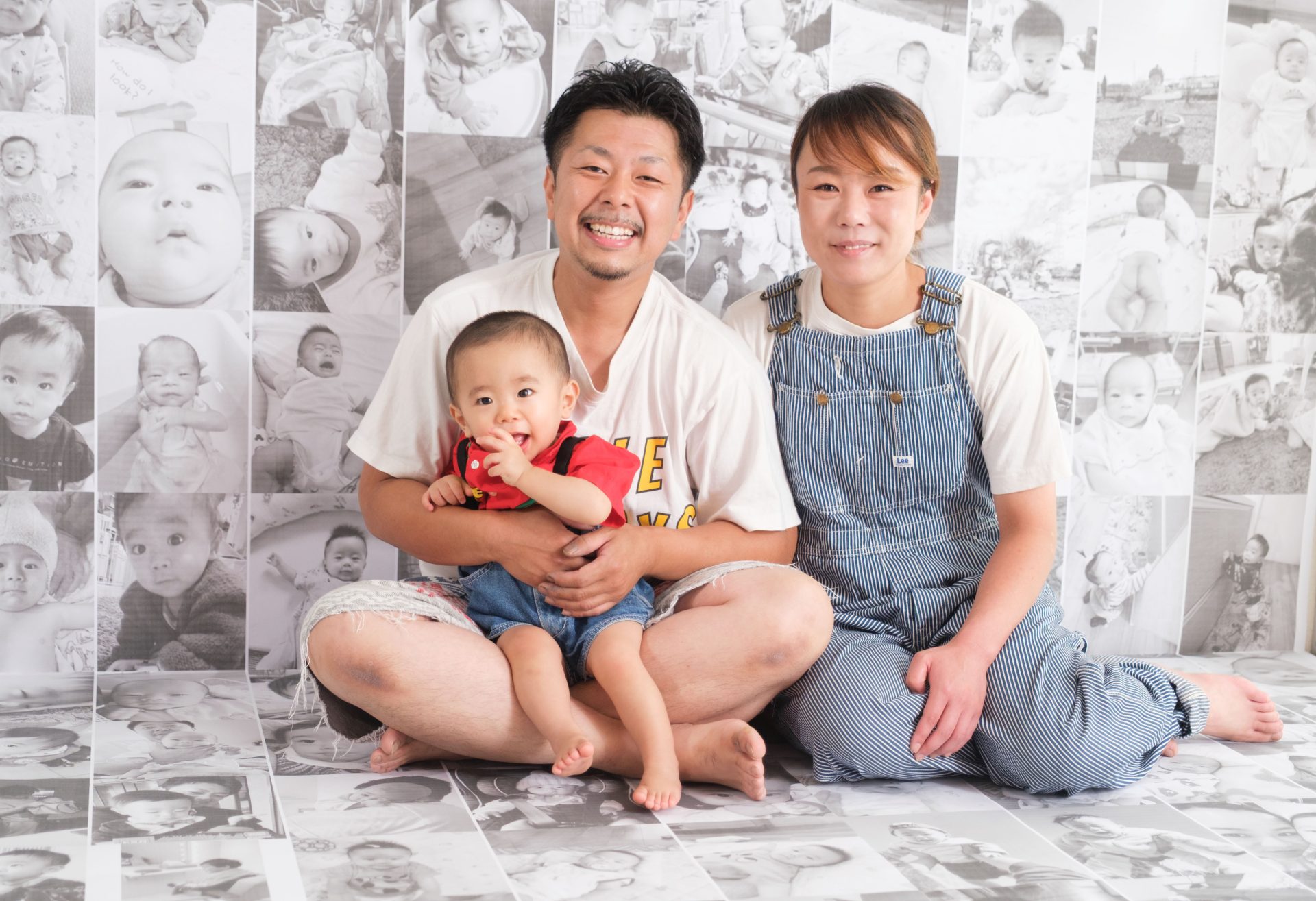 これまでの成長を撮りためてきて数々の写真をモノクロで並べて、その写真の前で１歳近年の家族写真