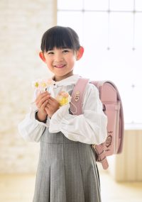 ランドセルを背負い、桜の花を手に微笑む女の子