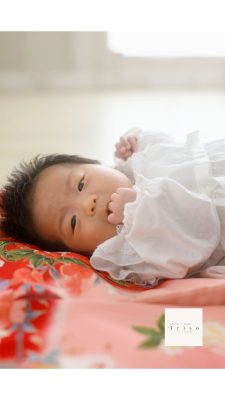 赤い着物の上に可愛い女の子の赤ちゃんが寝転んでいる
